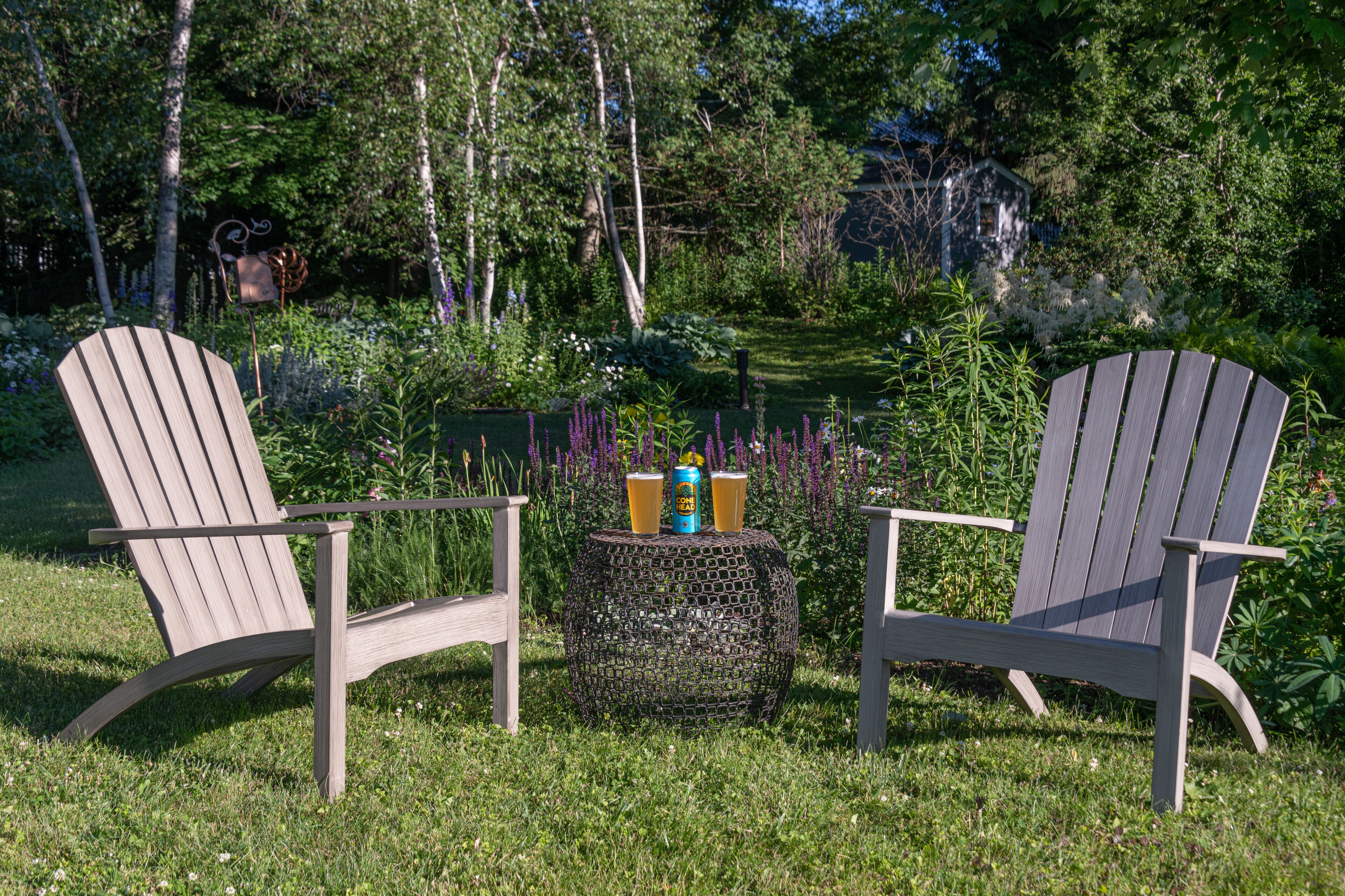 Dos sillas Adirondack con una mesa redonda en un exuberante jardín.
