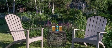 Dos sillas Adirondack con una mesa redonda en un exuberante jardín.