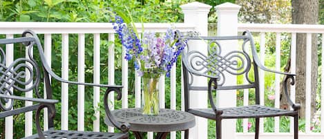 A patio with two metal chairs and a table, surrounded by a white fence and lush greenery.