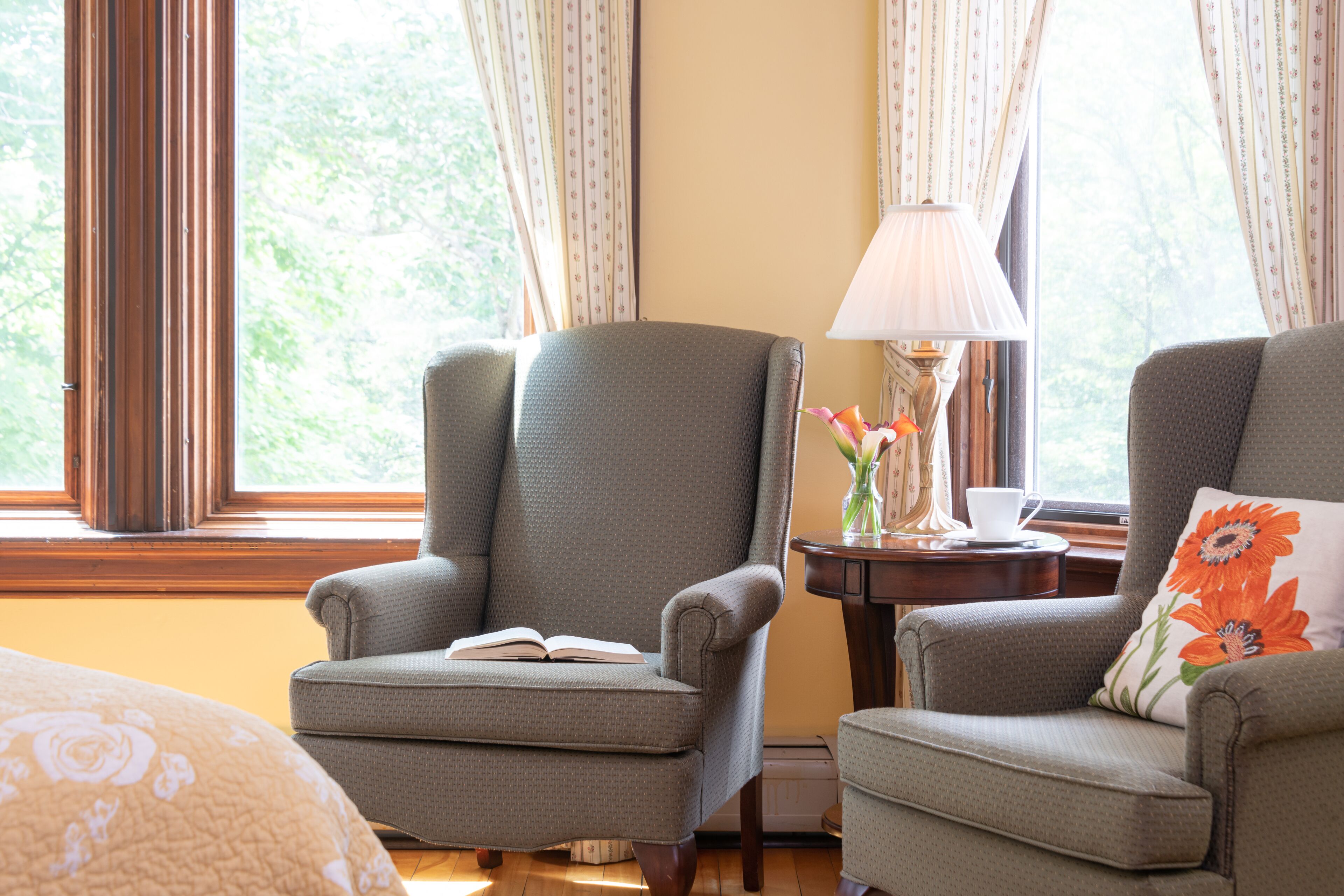 A room with two armchairs, a table with a lamp, and a window with curtains.