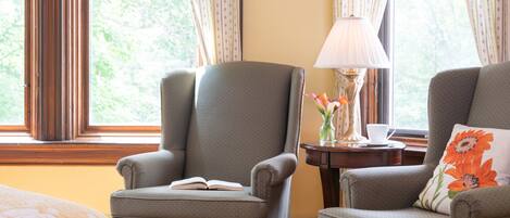 A room with two armchairs, a table with a lamp, and a window with curtains.