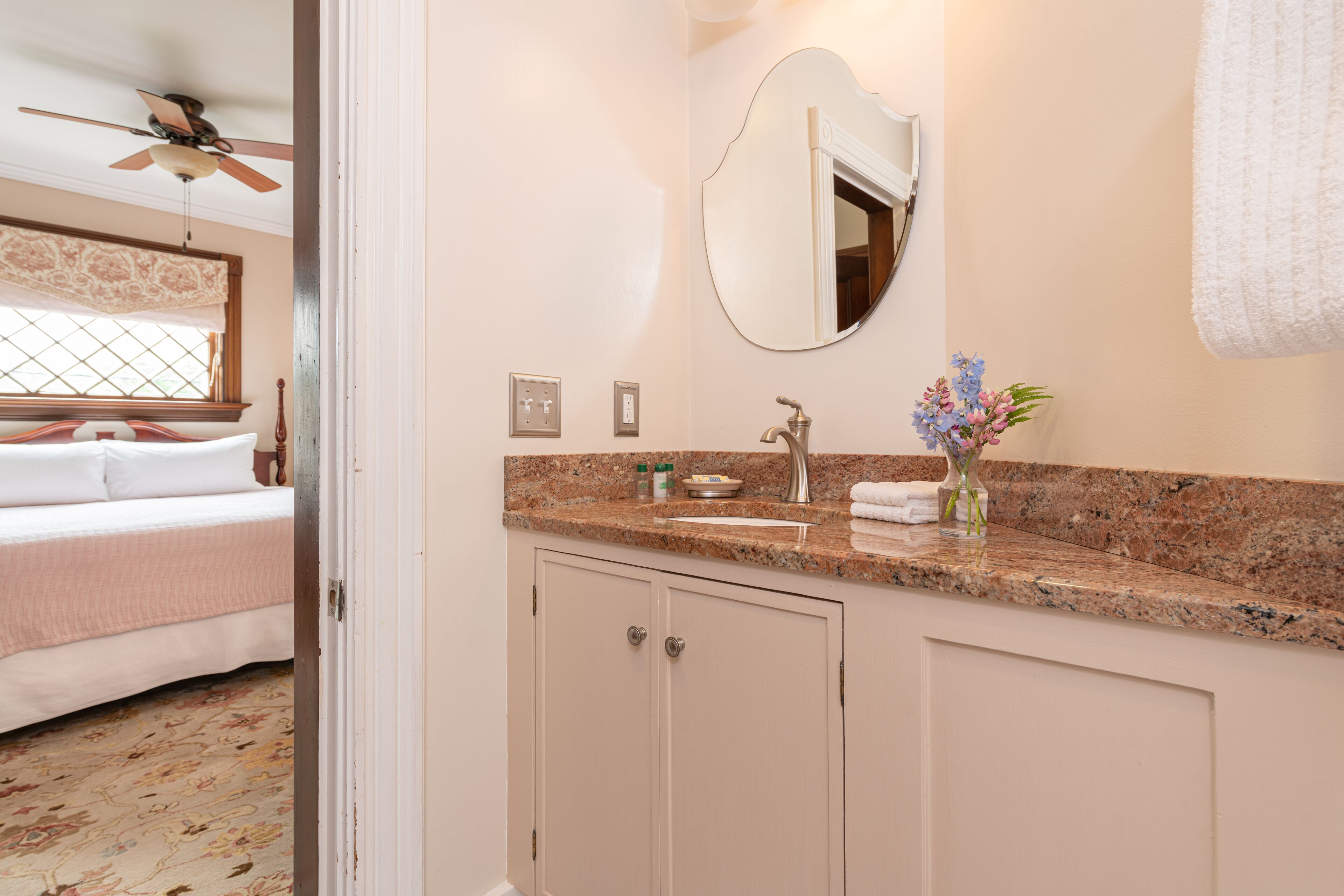 Ein Badezimmer in einem Hotel mit einer Arbeitsplatte aus Granit, einem Waschbecken, einem Spiegel und einer Vase mit Blumen.