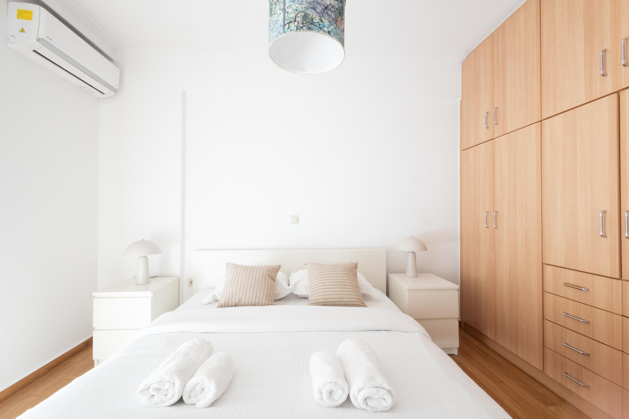 Une chambre d’hôtel au design minimaliste, comprenant un lit, une armoire en bois, des tables de chevet et un appareil de climatisation.