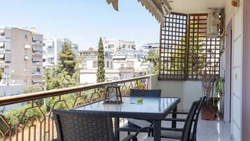 Un balcon avec une table et des chaises, un pot de fleurs et une vue sur les bâtiments environnants.