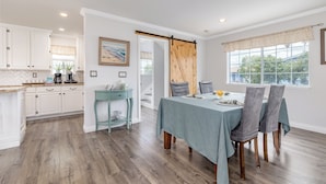 A dining area with a table set for four, a sliding barn door, and a view of the outdoors through a window. - Stunning, Beach Home near Santa Cruz Beach & Boardwalk, Walk Downtown! Superhost (Santa Cruz)