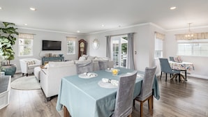 A spacious living room with a dining area, featuring a large window, a chandelier, and a television. - Stunning, Beach Home near Santa Cruz Beach & Boardwalk, Walk Downtown! Superhost (Santa Cruz)