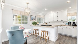 A bright kitchen with white cabinets, a central island, and wooden stools. - Stunning, Beach Home near Santa Cruz Beach & Boardwalk, Walk Downtown! Superhost (Santa Cruz)