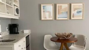 A modern kitchen with white cabinetry, a coffee maker, and a dining area with two chairs and a round table.