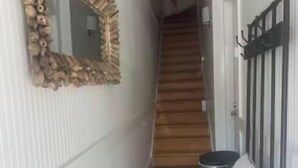 A narrow hallway with a wooden staircase, a bench, and a decorative mirror on the wall.