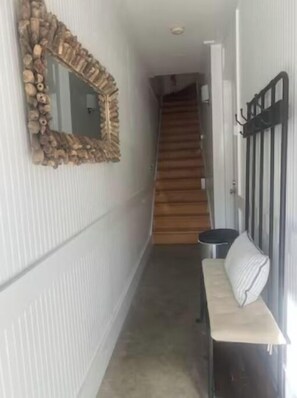 Staircase leads to an upper floor, flanked by a bench and a leaf-shaped mirror.