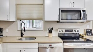 Una cocina moderna con armarios blancos, un microondas de acero inoxidable, un lavavajillas y una estufa.