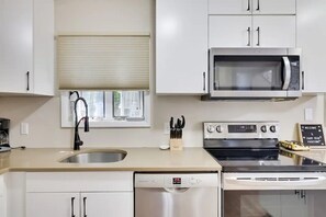 Une cuisine moderne avec des meubles blancs, un four à micro-ondes en acier inoxydable, un lave-vaisselle et une cuisinière.
