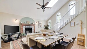 Un salón espacioso con chimenea, un comedor listo para cuatro personas y una escalera que sube a un nivel superior.