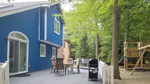 Una casa azul con terraza, muebles de exterior y un parque infantil de madera.