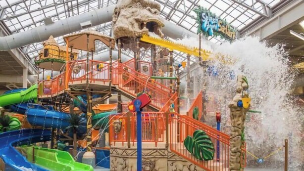 Parque acuático interior con toboganes, una torre de salpicaduras y una zona de juegos temática de la selva.