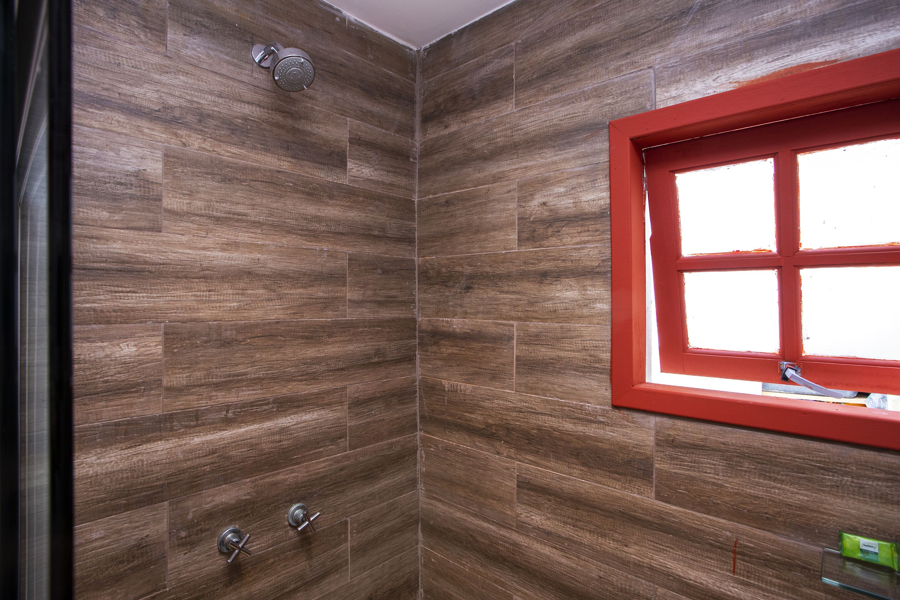 Une douche avec une fenêtre à cadre rouge, des murs en bois et une pomme de douche en métal.
