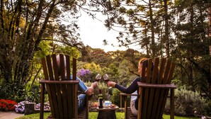 Deux chaises en bois, placées face à face, avec une table entre elles, dans un jardin agrémenté de diverses plantes et fleurs.