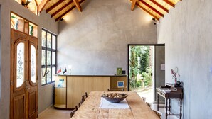Un grand espace dédié à la salle à manger, avec une longue table en bois, un saladier rempli de fruits et un comptoir en bois sur lequel se trouve un ordinateur.
