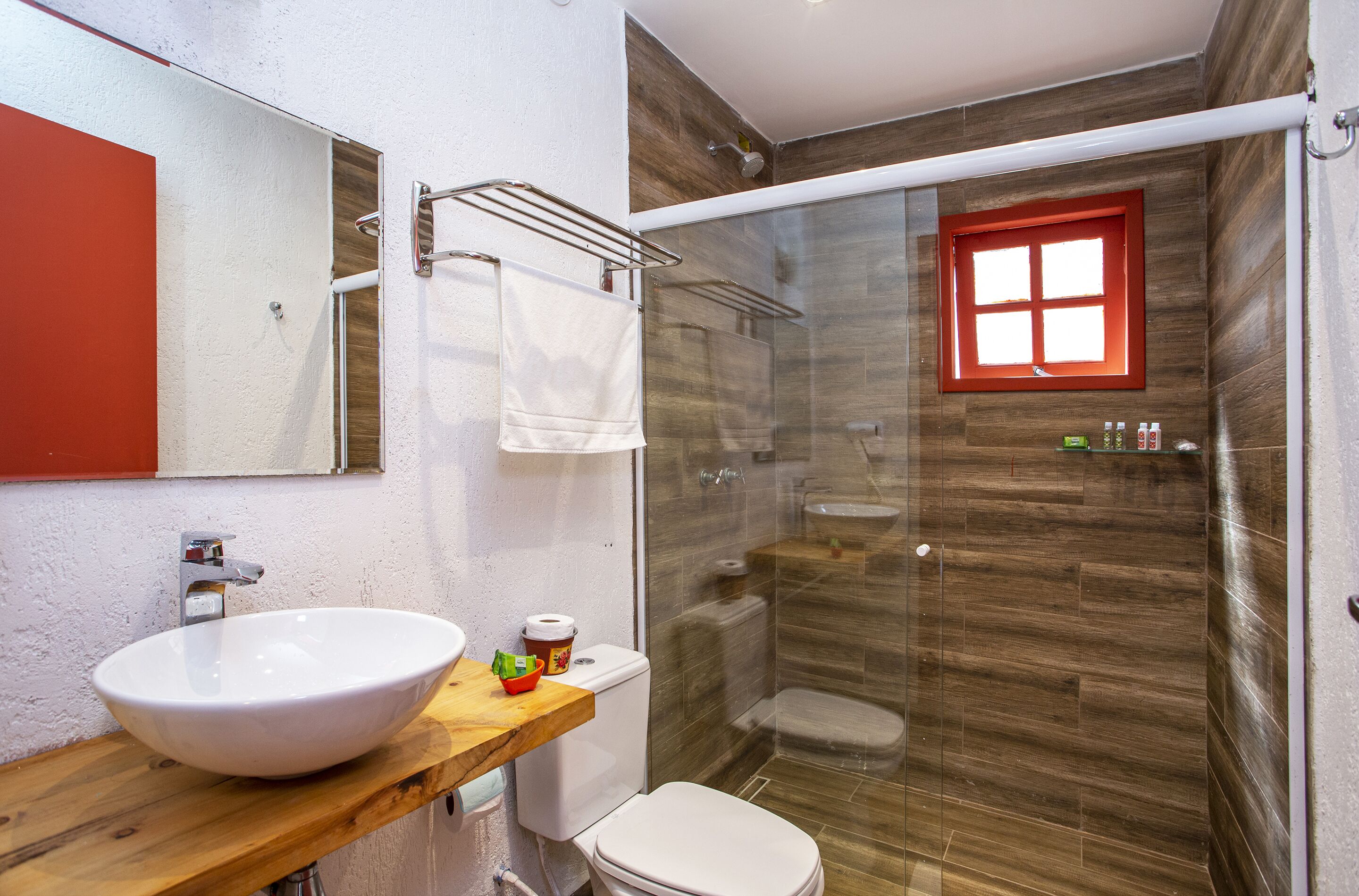 Un baño con tocador de madera, lavamanos blanco, inodoro y cabina de ducha con paredes de vidrio.