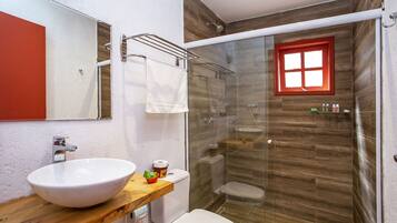 Un baño con tocador de madera, lavamanos blanco, inodoro y cabina de ducha con paredes de vidrio.