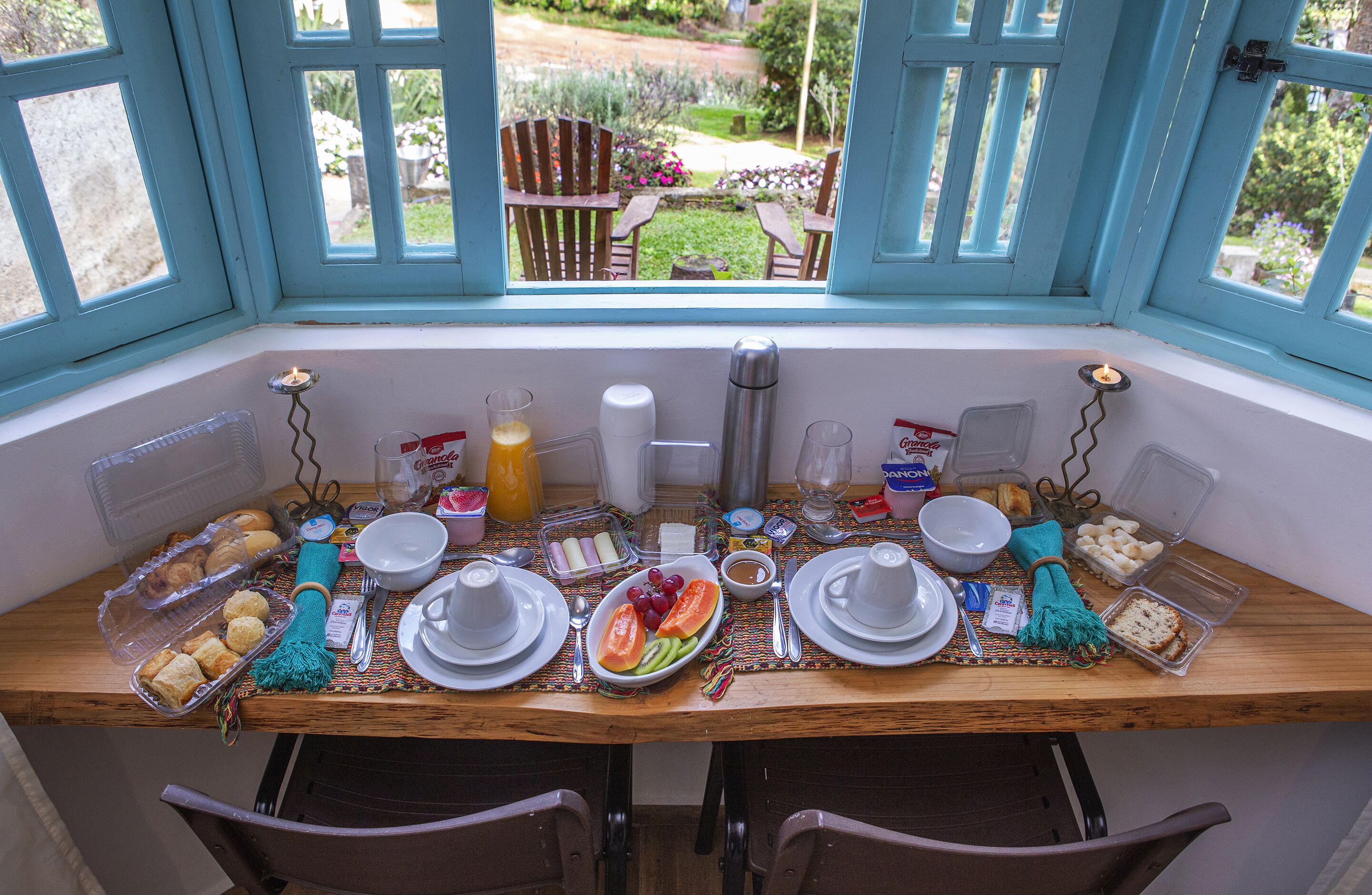 A breakfast setup with a table set for two, including plates, cups, and a variety of food items.