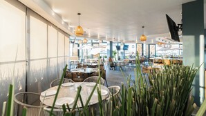 Un espace de restauration intérieur avec des tables rondes, des chaises en osier et des lampes suspendues.