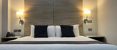 Una habitación de hotel con una cama grande, dos mesitas de noche, un teléfono y lámparas fijadas a la pared.