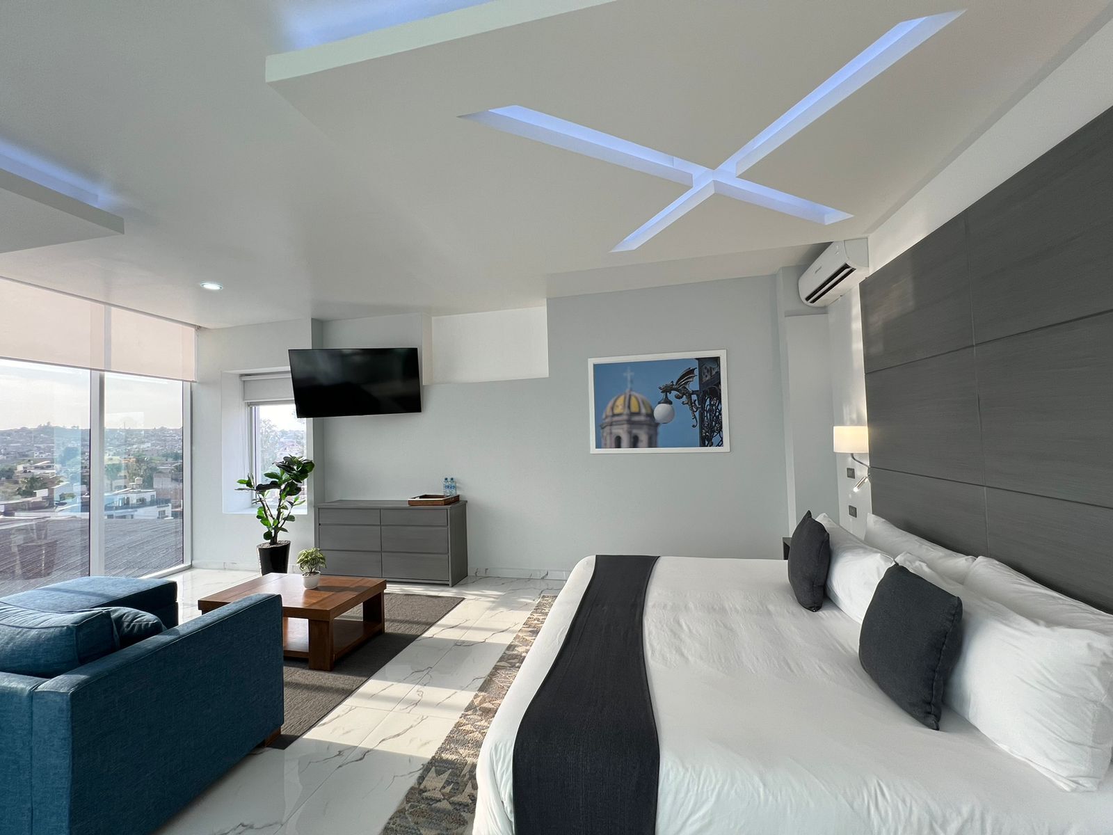 Quarto de hotel moderno com uma cama grande, um sofá, uma TV, uma escrivaninha e vista para a cidade.