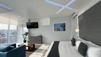 Quarto de hotel moderno com uma cama grande, um sofá, uma TV, uma escrivaninha e vista para a cidade.
