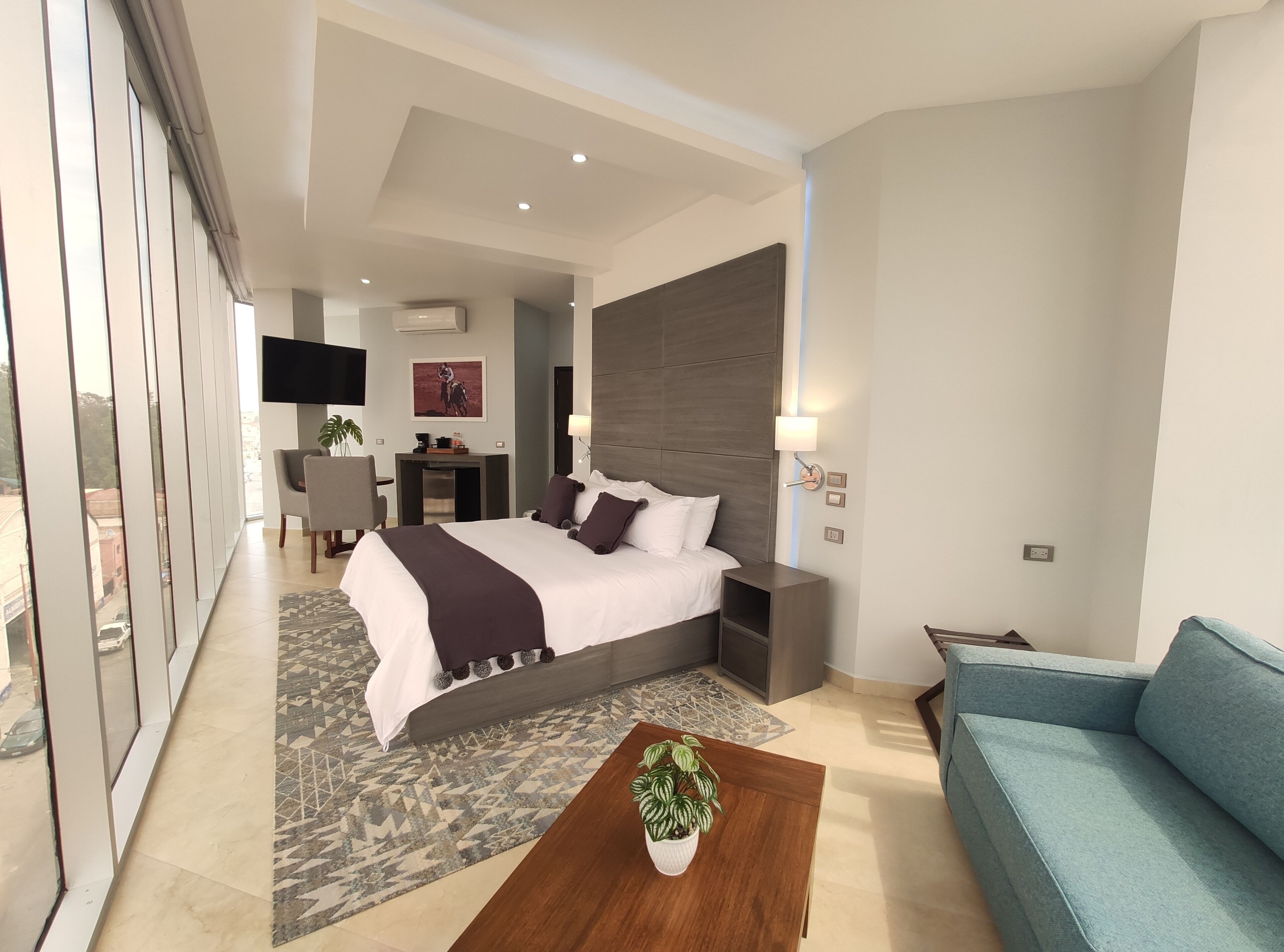 A modern hotel room with a large bed, a desk, a TV, and a sofa.