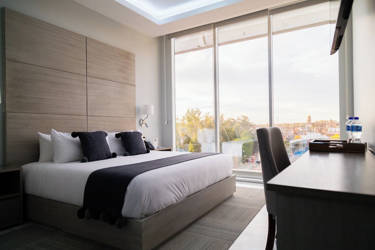 A modern hotel room with a large bed, a desk, and a city view through the window.