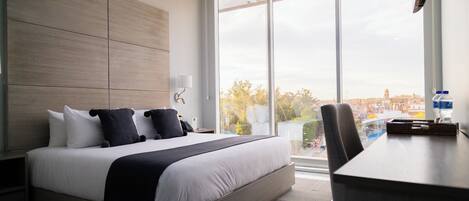 Una habitación de hotel moderna con una cama grande, un escritorio y vistas a la ciudad desde la ventana.