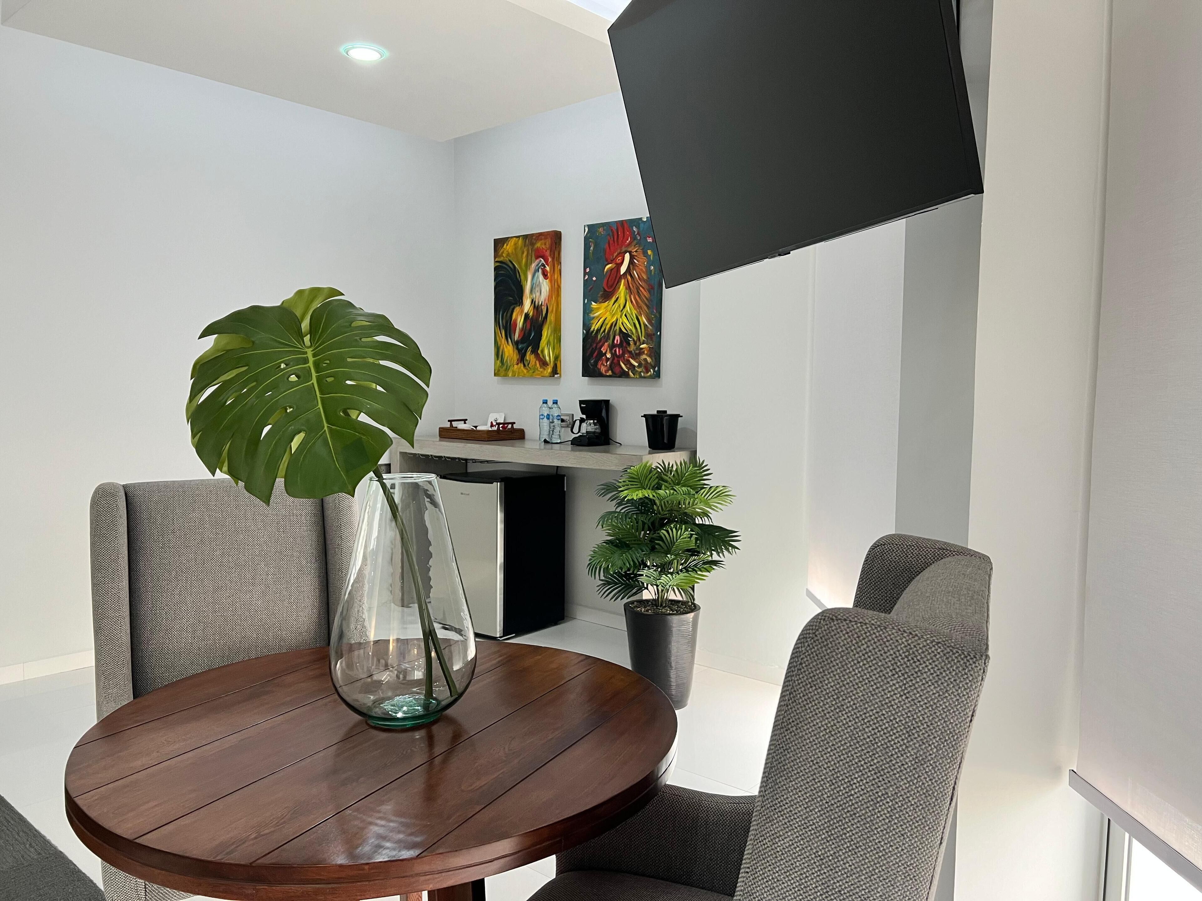A modern dining area with a round wooden table, two grey upholstered chairs, a glass vase with a plant, and a potted plant.