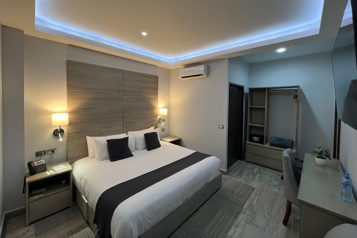 A modern hotel room with a large bed, bedside tables, a desk, and a wardrobe.