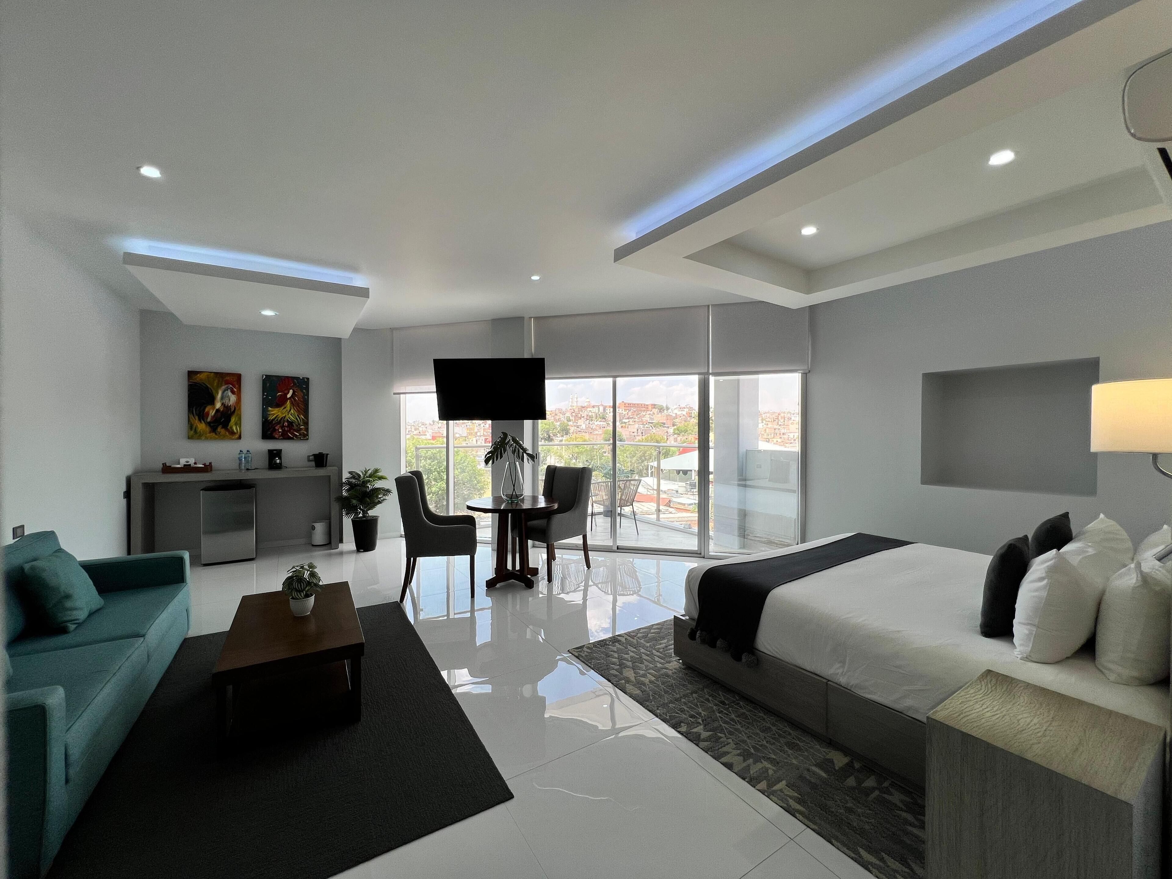 Une chambre d’hôtel moderne dotée d’un grand lit, d’un canapé, d’un bureau avec un téléviseur à écran plat et d’un balcon offrant une vue sur la ville.