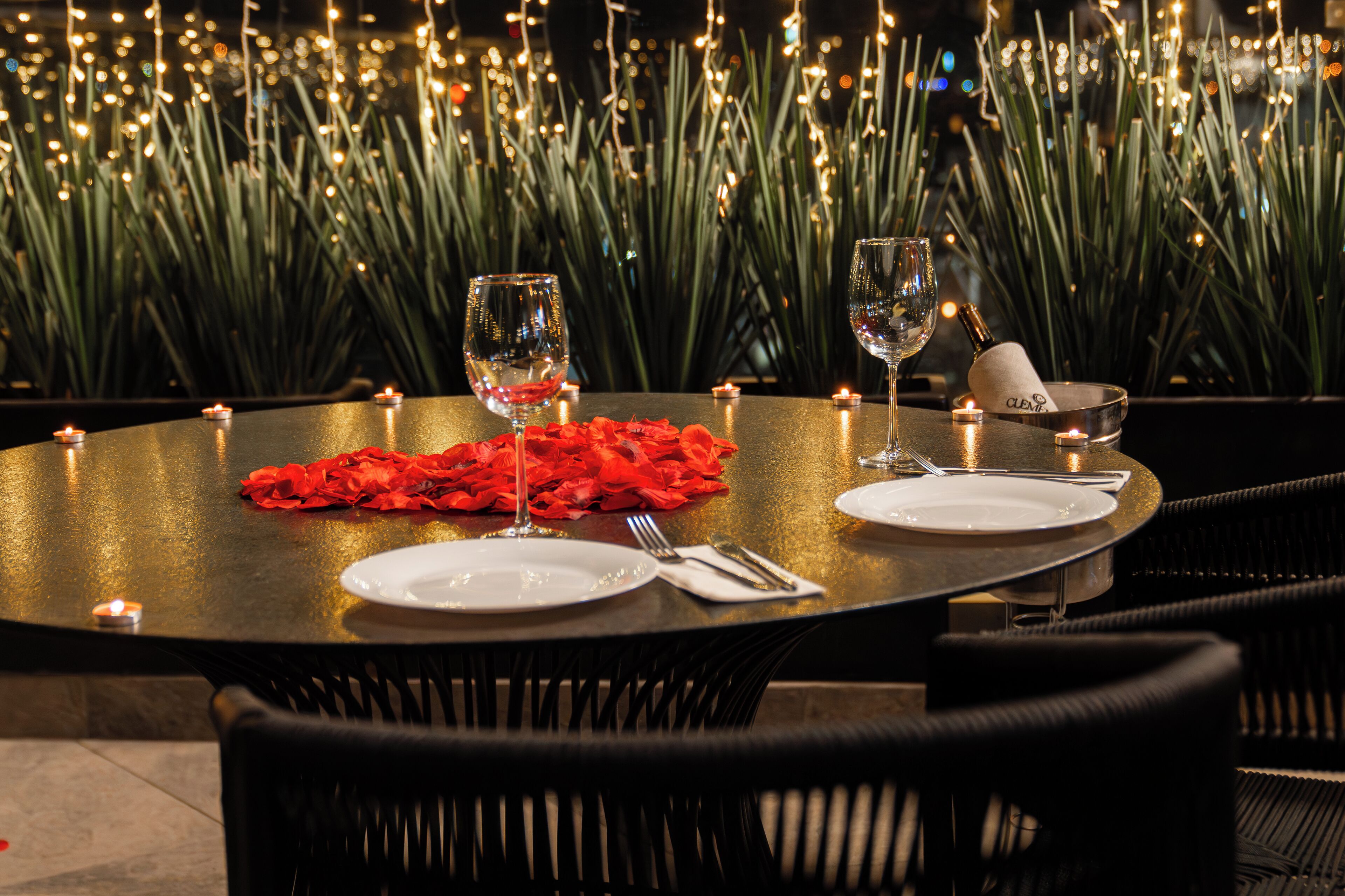 A round dining table set with candles, a red rose, wine glasses, and cutlery.