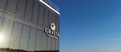 Um hotel moderno com fachada de vidro refletiva, um logotipo em destaque e a inscrição 'GRALTA CHAVEZ HOTEL'.