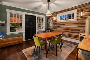 Un comedor con una mesa y sillas de madera, una lámpara colgante y vistas al exterior a través de ventanas amplias.