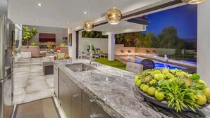 A modern kitchen with a marble countertop, a built-in sink, and a dining area with a pool view. - Troy Dr - Sleek & Modern Hollywood Hills Home With Stunning Views (Los Angeles)