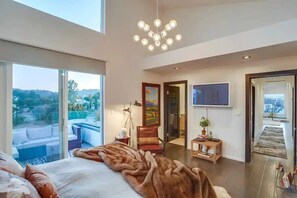 A modern bedroom with a large bed, a view of the outdoors, a chandelier, and a television. - Troy Dr - Sleek & Modern Hollywood Hills Home With Stunning Views (Los Angeles)