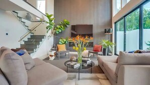 A modern living room with a staircase, a coffee table with books, and a vase with flowers. - Troy Dr - Sleek & Modern Hollywood Hills Home With Stunning Views (Los Angeles)