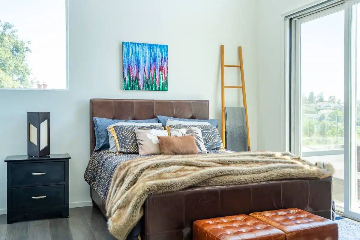 A bedroom with a large window, a bed with a fur throw, a wooden ladder, and a nightstand.
