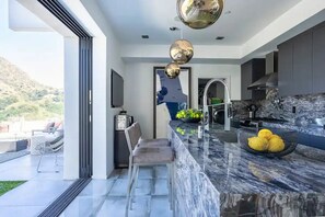 A modern kitchen with a marble countertop, stainless steel appliances, and a view of a mountainous landscape. - Troy Dr - Sleek & Modern Hollywood Hills Home With Stunning Views (Los Angeles)