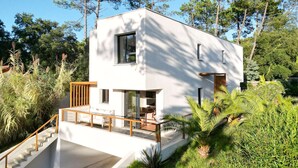 A modern two-story house with a white exterior, a wooden deck, and a staircase leading to the entrance. - Villa ALOITA (SEIGNOSSE)