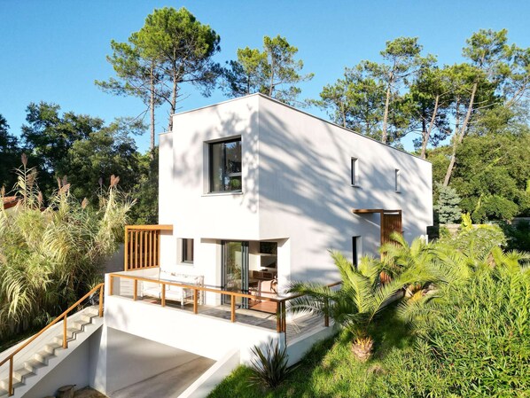 A modern two-story house with a white exterior, a wooden deck, and a staircase leading to the entrance. - Villa ALOITA (SEIGNOSSE)