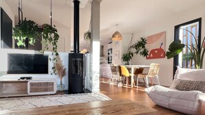 A modern living room with a TV, a black wood-burning stove, and a dining area with chairs and a table. - Villa ALOITA (SEIGNOSSE)