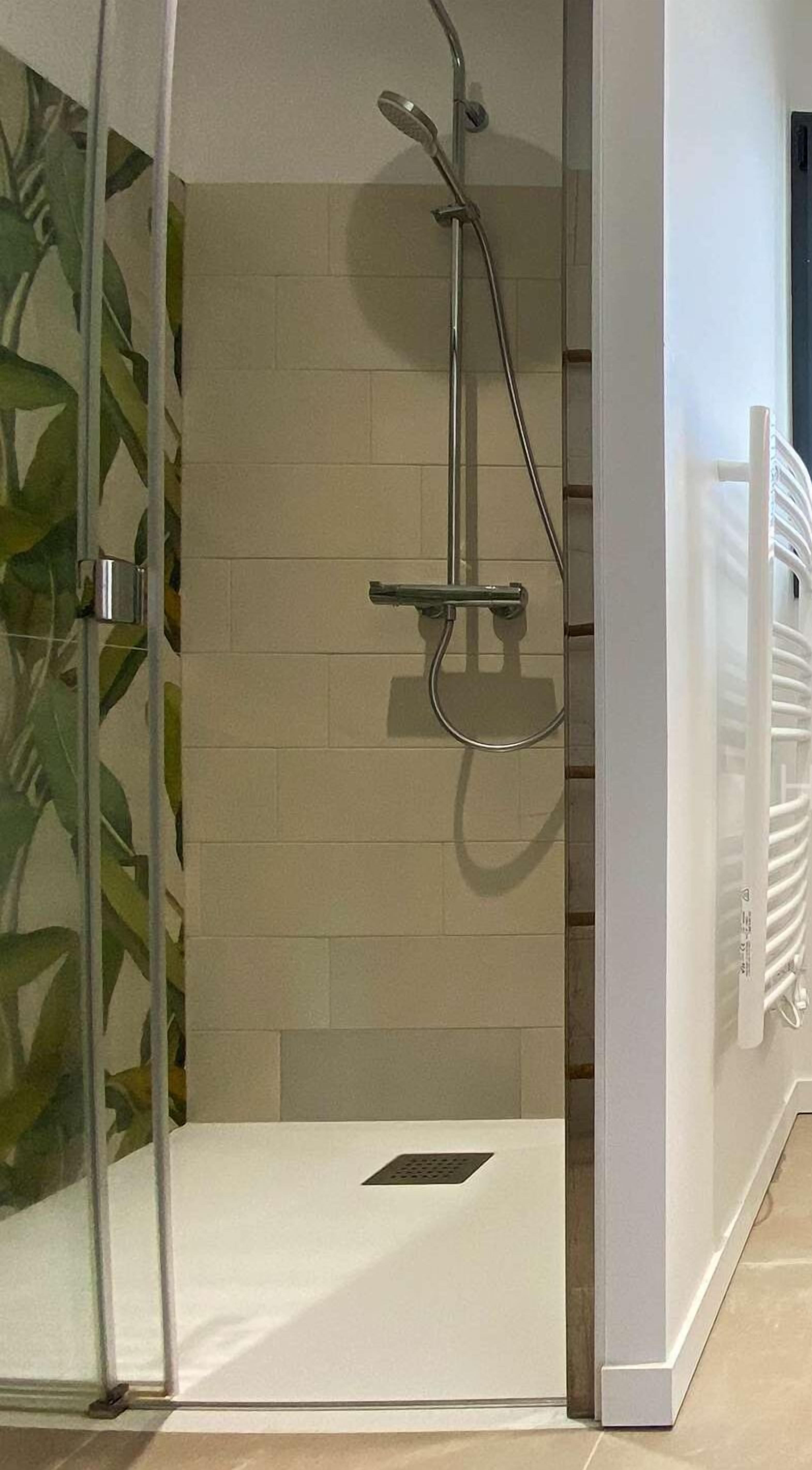 A glass-enclosed shower area with a tiled wall, a showerhead, and a control panel.