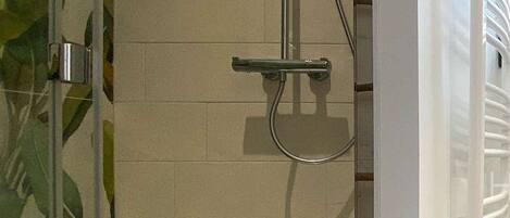 A glass-enclosed shower area with a tiled wall, a showerhead, and a control panel.