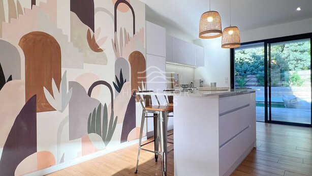 A modern kitchen with a large island, pendant lights, and a view of the outdoors. - Villa ALOITA (SEIGNOSSE)