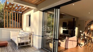 A modern interior with a wooden deck, a sofa, a dining area, and a sliding glass door leading to a garden. - Villa ALOITA (SEIGNOSSE)